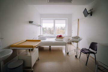 Clean hospital room with a bed, changing table, baby bassinet, chair, and window with a view of trees, designed for patient comfort and care.