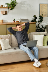 Fototapeta premium A handsome young man relaxes on the couch with his laptop in a cozy setting.
