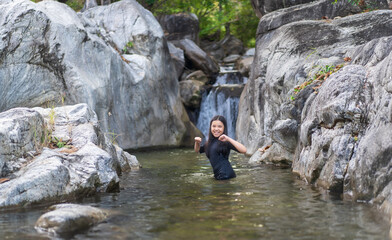 asian child playing waterfall or kid girl happy smile standing in natural water with rocks stones or young people in pool nature stream in summer and forest for holiday travel adventure at lan sang