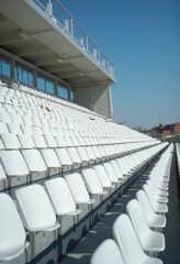 Fototapeta premium White tribunes. seats of tribune on sport stadium. empty outdoor arena. concept of fans. chairs for audience. cultural environment concept. color and symmetry. empty seats. modern stadium