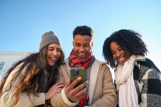 Three young students are having fun watching something on a smartphone in winter