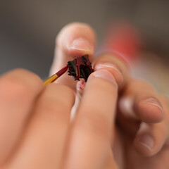 Close-up photograph of painting a part of a wargaming model with red paint. The image focuses on the brush, the model's surface, and the fine details being applied.