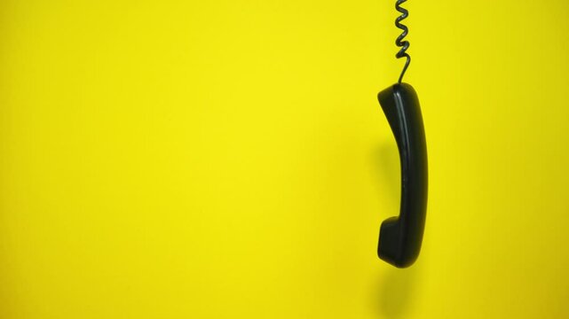 Old black telephone handset hanging on a yellow background