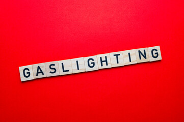 Word Gaslighting, written with wooden alphabet blocks, on red surface.