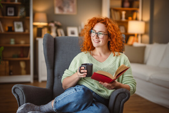 beauty redhead woman sit in the armchair and enjoy at coffee and book