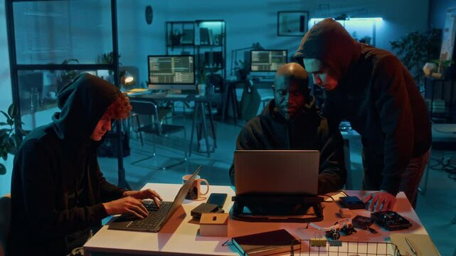 Three diverse male cyberthreat actors attacking IT resources of company while working on laptops in office