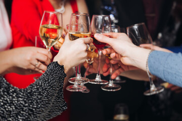 Group of guests celebrate and raise glasses, toasting and cheering with alcohol glasses with wine and champagne in the restaurant on corporate christmas birthday party event or wedding celebration