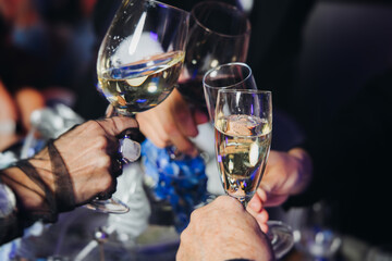 Group of guests celebrate and raise glasses, toasting and cheering with alcohol glasses with wine and champagne in the restaurant on corporate christmas birthday party event or wedding celebration