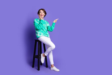 Full size photo of attractive young woman sit chair point empty space dressed stylish green clothes isolated on violet color background