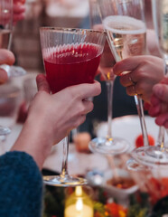 Group of guests celebrate and raise glasses, toasting and cheering with alcohol glasses with wine and champagne in the restaurant on corporate christmas birthday party event or wedding celebration