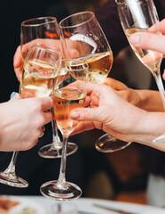 Group of guests celebrate and raise glasses, toasting and cheering with alcohol glasses with wine and champagne in the restaurant on corporate christmas birthday party event or wedding celebration