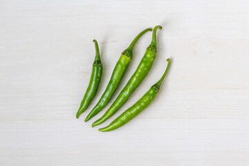 Fresh green chili peppers of varying sizes on a light wooden backdrop, viewed from above.