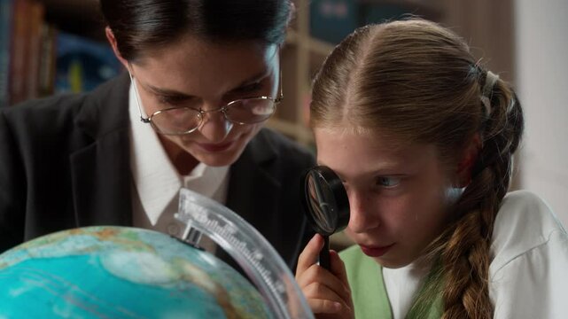 Professor female Caucasian professional tutor woman teacher explaining discuss teaching educating little girl school child kid student learner studying globe earth world map use magnifier in classroom