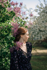 red-haired girl in a purple dress near blooming lilacs