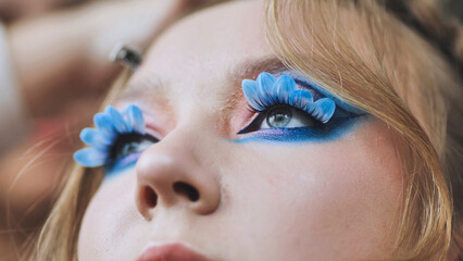 Makeup artist applying vibrant blue petal shaped false lashes, creating dramatic eye makeup for fashion photoshoot