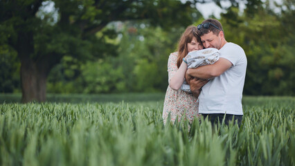 Loving parents cuddling newborn amid lush green meadow, sharing tender family connection