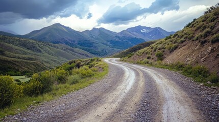 Fototapeta premium Winding gravel road through mountainous terrain ideal for off-road adventures and rallying under a dramatic sky with lush greenery.