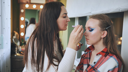 Skilled makeup artist applying bold, colorful eyeshadow on model's eyelids during professional beauty salon photoshoot