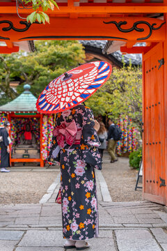 View of lady in Kimono with colourful umbrella in street near Torii gate in Gion, KKyoto Geisha District, Kyoto, Honshu, Japan