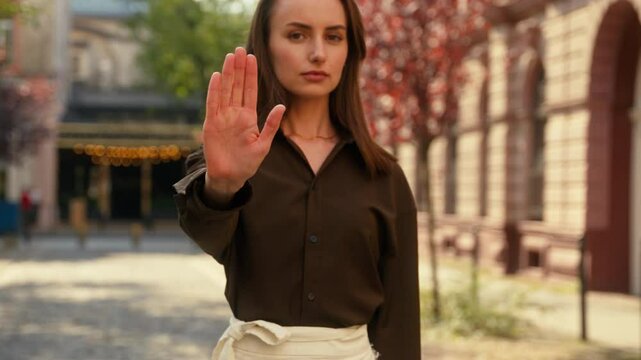 Confident serious Caucasian woman girl female lady businesswoman stylish business looking at camera stop palm in front not forbid keep distance limit no refuse reject deny border ban in city outdoors
