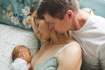 Young mother breastfeeding her newborn baby son. Happy father looking at them. Breast feeding and...