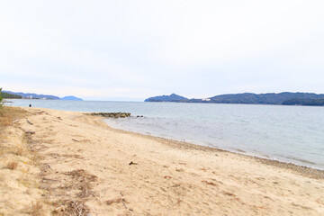 Sandy Beach Shoreline with Distant Mountains and Blue Sky, Amanohashidate Sandbar, Kyoto, Japan

