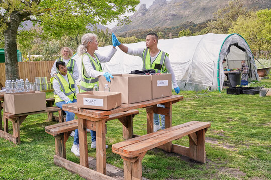 Two volunteers doing high five over donation boxes at table outdoors