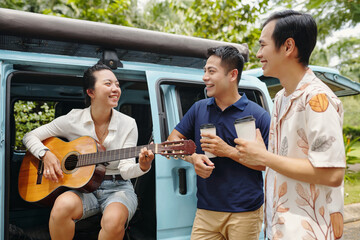Young woman playing guitar for her friends while they travelling in nature