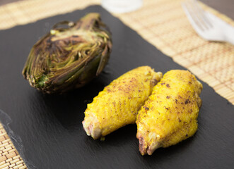 Cooked fried chicken wings and halves artichokes on black stone plate
