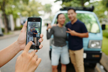 Close-up of man photographing couple against van on his smartphone