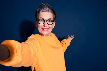 Photo of attractive mature woman selfie photo point hand empty space dressed stylish yellow clothes isolated on dark blue color background