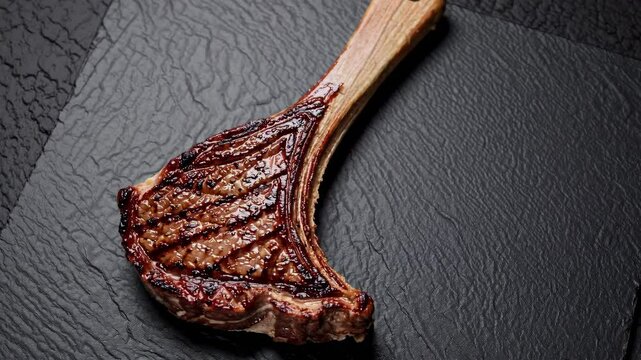 Grilled tomahawk steak on black slate surface, gourmet dining presentation. Culinary arts and food styling concept