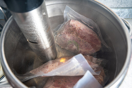 Thermal immersion circulator and vacuum packed meat in pot on white background. Sous vide cooking