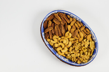 Assorted nuts in a stoneware container with a straw basket, on a white background. Almonds, Walnuts, Cashews and Chestnuts