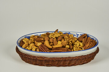 Assorted nuts in a stoneware container with a straw basket, on a white background. Almonds, Walnuts, Cashews and Chestnuts