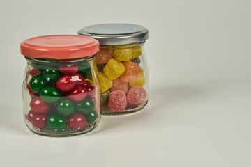 Jelly candies and dipped chocolates, in various bright and vivid colours, in suitable containers, on a white background.