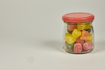 Appetizing and colorful jelly candies, coated with sugar, in a container on a white background