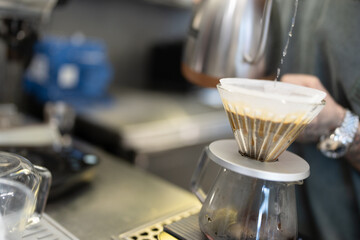 Professional barista making filtered drip coffee in coffee shop. Close up of hands barista brewing a drip hot espresso coffee, pour over coffee with hot water and filter paper in coffee cafe.