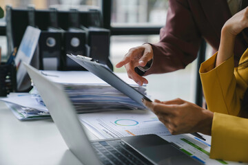 Business team working with financial data analyzing charts and graphs discussing project strategy using laptop and clipboard