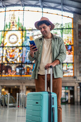 vertical latin Tourist using smartphone and carrying trolley suitcase at train Station