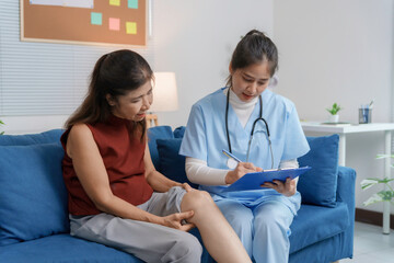 Asian female doctor visiting senior patient and writing notes about knee pain on clipboard during...