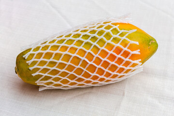 Whole papaya fruit in fruit packaging net on a table