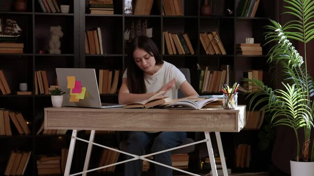 Student who studied late sleeps with her head on the table over the pile of books and notebooks. Young woman tired from studying a lot without breaks. Girl studies in a modern library