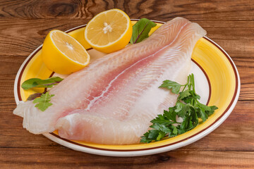 Pangasius fillet on yellow dish with lemon on rustic table