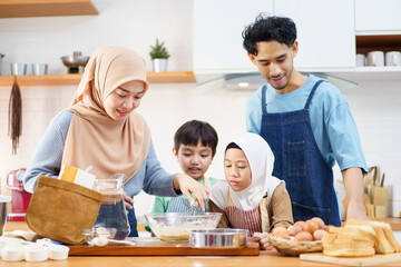 Happy Asian muslim family consisting father, mother, son, and daughter are cooking together in the kitchen.