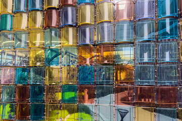 Stained colorful transparent glass parts decorative wall illuminated on light, design installation multicolor acrylic panels or tiles hanging in garden, abstract background.