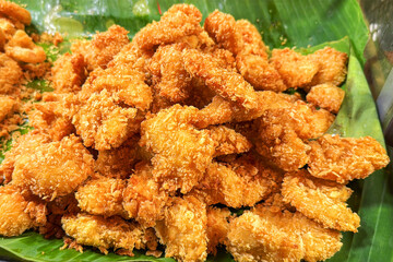 Street fast food breaded fried chicken fillet, crispy nuggets roasted in hot oil, strips, meat pieces in breadcrumbs on green banana leaf plate on market close-up.