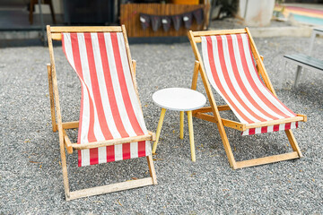 Red white striped timber beach deck chair on gravel sea shore or back yard garden, outdoor furniture, relax lounge calm patio place with seats, summer vacation, travel.