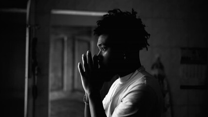 Profile of a devout young black man in PRAYER at home in monochromatic. Artistic black and white clip of religious African American person asking for God's intervention