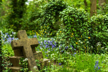 Old Cross Gravestone Surrounded by Wildflowers in Lush Green Cemetery